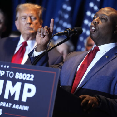 FILE - Republican presidential candidate former President Donald Trump listens as Sen. Tim Scott, R-S.C., speaks at a primary election night party at the South Carolina State Fairgrounds in Columbia, S.C., Saturday, Feb. 24, 2024. (AP Photo/Andrew Harnik, File)